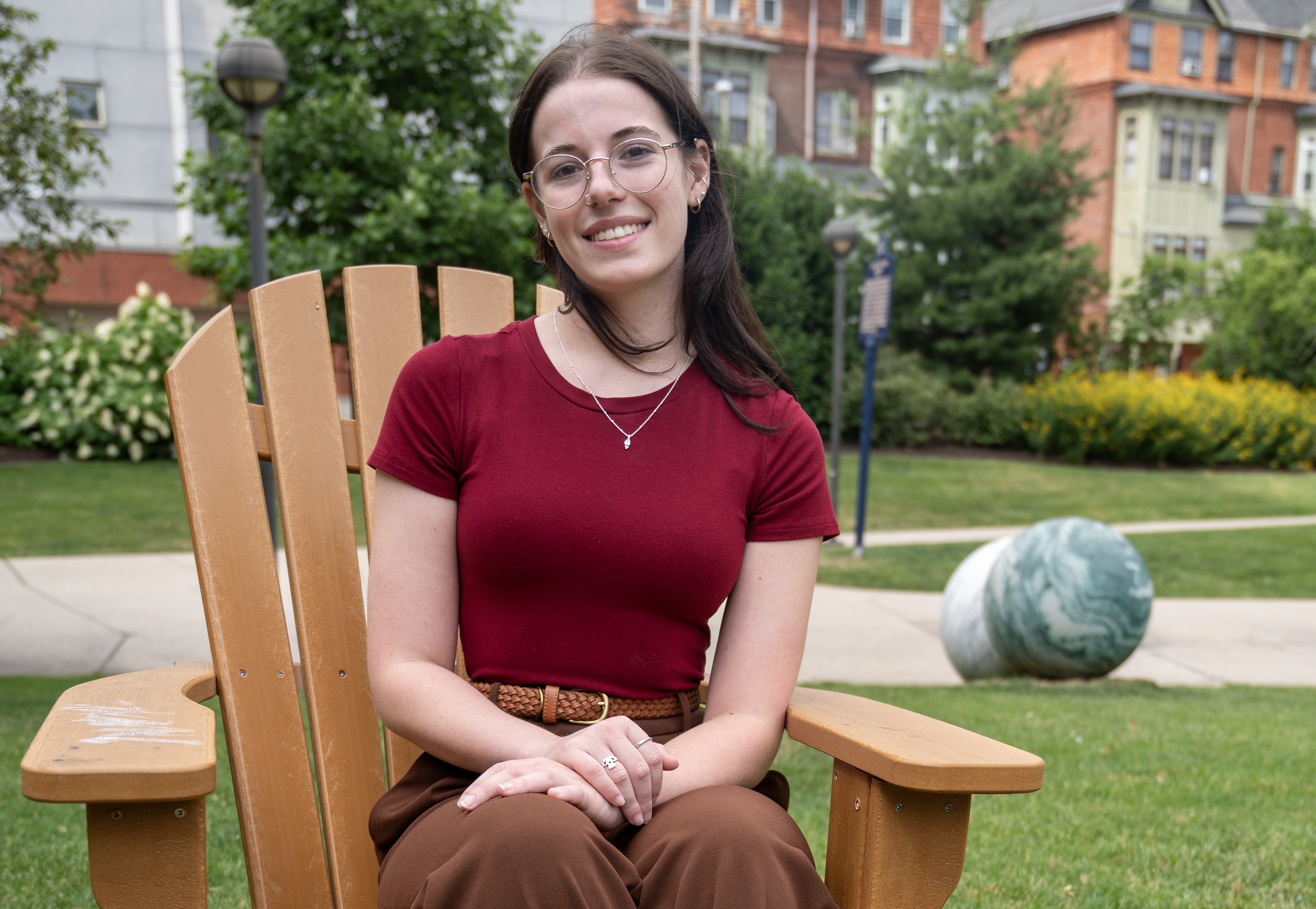 Stephanie Bieder wearing red shirt and brown pants sitting in brown adirondack chair